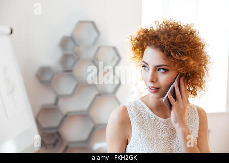Pensativo joven y bella mujer de negocios hablando por teléfono celular en la oficina Foto de stock