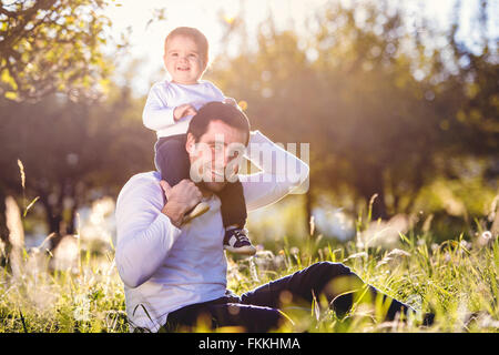 Hijo de padre llevar sobre los hombros, sentarse en la hierba Foto de stock