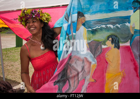 Mujer con flor de Polinesia tocado mostrando un estilo Gaugain pareu tela para la venta en un mercado, Atuona, Hiva Oa, Islas Marquesas, en la Polinesia Francesa, Pacífico Sur Foto de stock