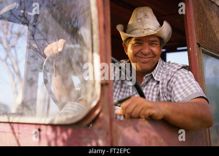 Y cultivos agrícolas en América Latina. Retrato de agricultores hispanos de mediana edad sentado orgulloso en su tractor al atardecer, holdi Foto de stock