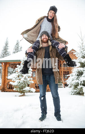 Hermosa pareja joven divirtiéndose cerca de la cabaña de troncos en invierno