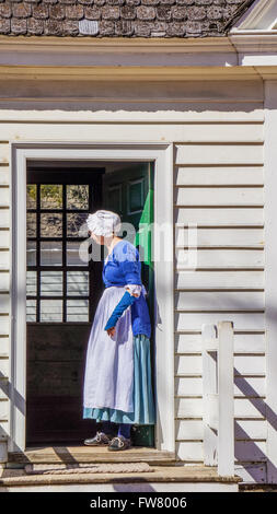 Mujer senior en Colonial Williamsburg en inglés tradicional vestido azul de pie en el umbral Foto de stock