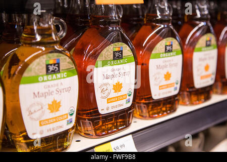 Un estante de botellas de jarabe de arce orgánico en la estantería de una tienda de comestibles. Foto de stock