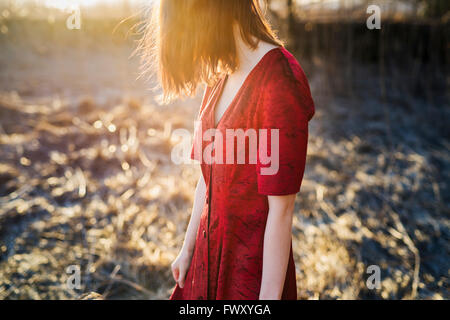 Finlandia, Varsinais-Suomi, joven mujer de pelo rojo en el vestido rojo de pie en la luz del sol
