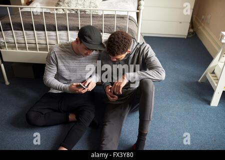 Dos estudiantes varones en dormitorio Comprobar mensajes en teléfonos móviles