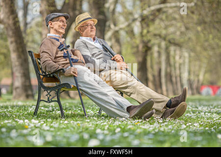 Dos altos señores sentarse y relajarse en un banco de madera en un parque en un día soleado Foto de stock