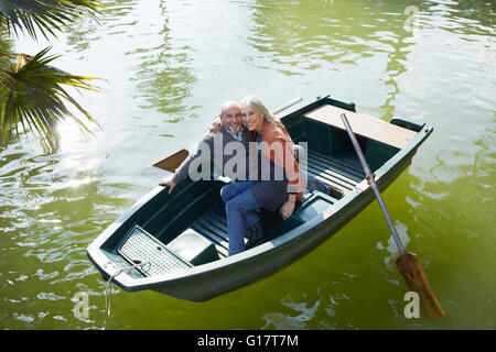 Pareja en bote a remo en el lago abrazando mirando a la cámara sonriendo Foto de stock