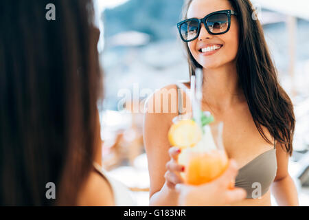 Alegre amigas bebiendo cócteles en verano y sonriente Foto de stock
