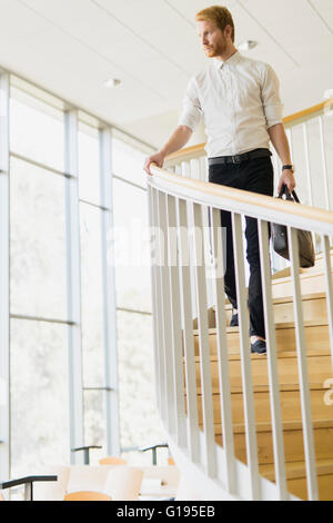 Guapo empresario bajando las escaleras sujetando una bolsa Foto de stock