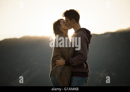 Romántico joven pareja besándose apasionadamente durante la puesta de sol, las montañas de fondo, sentimientos y relaciones concepto Foto de stock