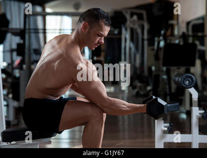 Muy power athletic guy culturista ejecutar el ejercicio con pesas en el gimnasio oscuro Foto de stock