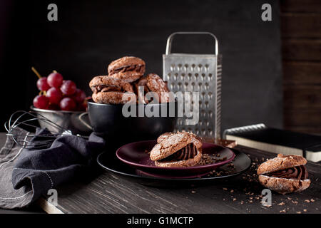 El italiano maroni cookies en el plato y el cuenco con las uvas, tela, portátil en el oscuro fondo antiguo de madera Foto de stock