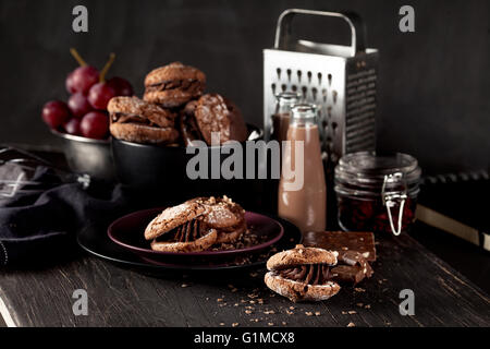 El italiano maroni cookies en el plato y el cuenco con las uvas, batidos de chocolate, tela, portátil en el oscuro fondo antiguo de madera Foto de stock