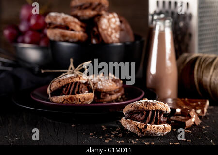El italiano maroni cookies en el plato y el cuenco con las uvas, batidos de chocolate, tela, portátil en el oscuro fondo antiguo de madera Foto de stock