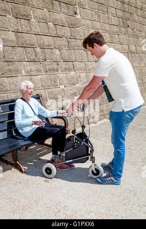Una anciana mujer discapacitada Levantarse de un banco, ayudado por su nieto, Brighton, Sussex, Reino Unido Foto de stock