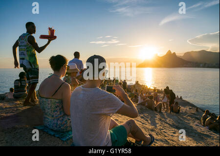 RIO DE JANEIRO - 26 de febrero de 2016: una multitud de personas se reúnen para ver la puesta de sol sobre las rocas en Arpoador en la playa de Ipanema. Foto de stock