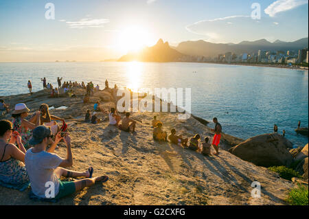 RIO DE JANEIRO - 26 de febrero de 2016: una multitud de personas se reúnen para ver la puesta de sol sobre las rocas en Arpoador. Foto de stock