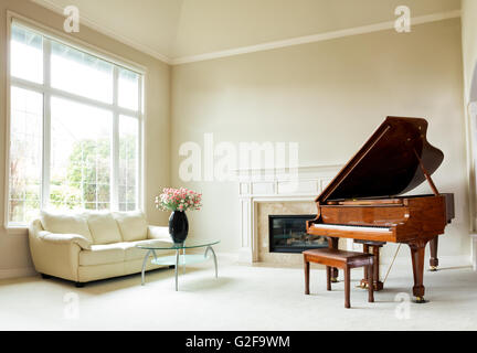 Salón con piano, chimenea, sofá y grandes ventanales con luz natural que entra a través de.