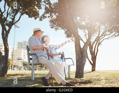 Disparó al aire libre de las parejas ancianas sentadas en un banco del parque con la mujer que muestra algo interesante a su marido. Pareja de jubilados
