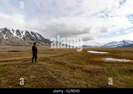 Un hombre está parado en la tundra ártica de Adventdalen, Longyearbyen, Spitsbergen, Svalbard, Noruega Foto de stock