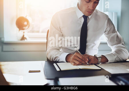 Primer plano de un hombre de negocios en camisa y corbata que trabajan en su oficina escribiendo en un cuaderno clásico Foto de stock