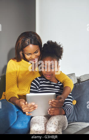 Poco chica negra y mamá con tablet sentado en el sofá sonriendo