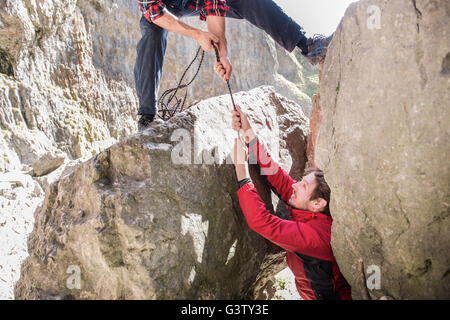 Dos montañeros se ayudan unos a otros durante una dura subida en un terreno escarpado. Foto de stock