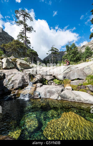 Joven sentado junto a una piscina con una pequeña cascada en las montañas, el río Golo, Parque Natural de Córcega