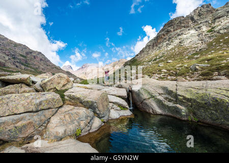 Joven de pie junto a una pequeña cascada con piscina en las montañas, el río Golo, Parque Natural de Córcega