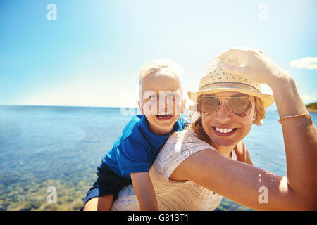 Feliz joven madre y su hijo en una playa tropical con la risa niñito obteniendo un piggy back ride sobre su espalda