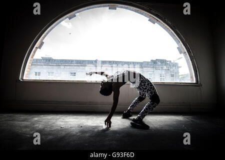 Belleza en abandono : Fitness y la fotografía de moda de una joven chica afro-caribeña doblando el ejercicio en semi-silueta delante de una ventana semicircular en un edificio abandonado abandonado UK Foto de stock