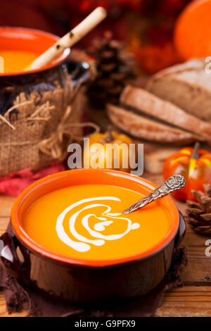 Un tazón de sopa de calabaza cremoso casero sobre una mesa rústica con decoraciones de otoño.