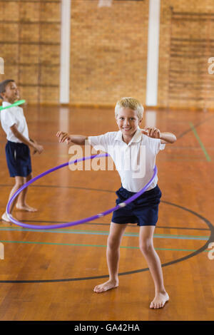 El colegial jugando con el hula hoop en el gimnasio de la escuela