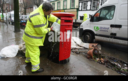 Un miembro del personal de Royal Mail limpia un buzón en el centro de la ciudad de Cockermouth después de las recientes inundaciones. Foto de stock