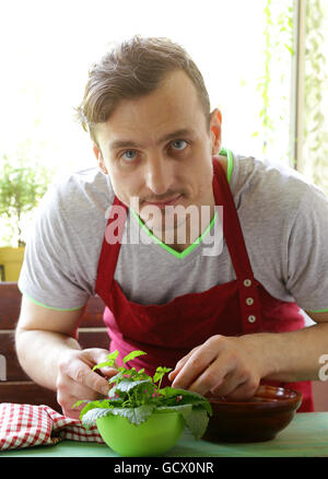 Hombre cocinar ensalada de verduras (tomates, lechuga, pepinillos) sobre una placa de madera Foto de stock