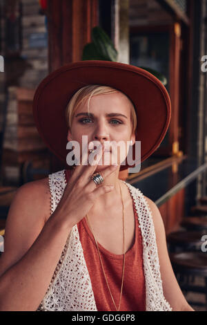 Retrato de mujer joven con sombrero de fumar un cigarrillo en una cafetería.