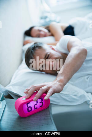 Hombre en la cama apagar el despertador por la mañana Foto de stock