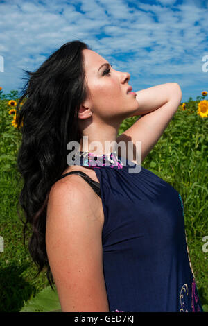 Bonita morena, joven, mujer de pie en el campo de girasol vistiendo vestido azul oscuro