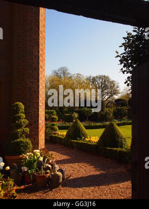 Vista vertical de camino a través de la puerta de Chenies Manor jardín con rincón de la casa con macetas y topiary en la tarde Foto de stock