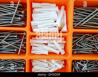 Tornillos y enchufes de pared en una caja de herramientas de plástico naranja Foto de stock