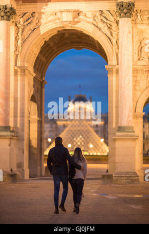 Un par en el Arc de triomphe du Carrousel & Palais du Louvre al atardecer, París, Francia