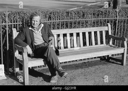 Un hombre sentado en un banco del parque de madera verde en Glasgow cerca del Palacio del Pueblo en 1972 Foto de stock