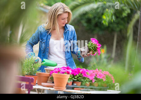 Mujer joven tiende la flor rosa de maceta en la mesa de jardín Foto de stock