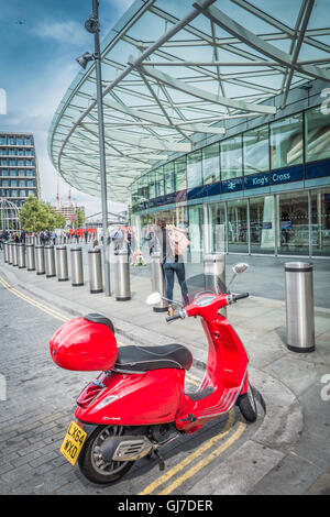 Londres, Inglaterra, REINO UNIDO: UN ferroviario de pasajeros que llegan a la estación de King's Cross en una Vespa scooter roja Foto de stock