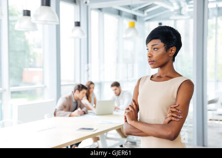 Pensativo empresaria joven afroamericano de pie con los brazos cruzados y pensar en la oficina
