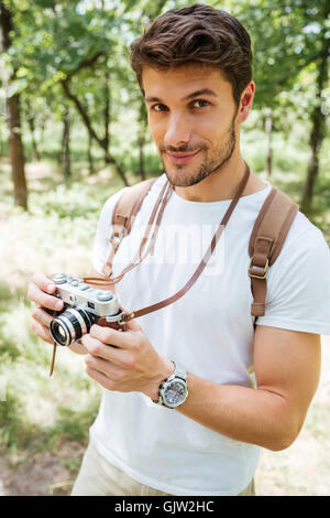 Apuesto joven con mochila para tomar fotos con la vieja cámara fotográfica en el bosque