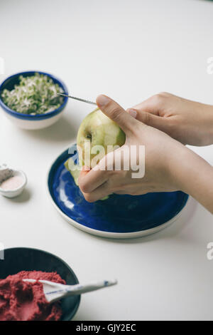 Chica slicing manzanas sobre una placa de color azul sobre un fondo blanco.