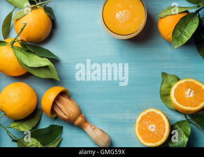 Jugo de naranja fresco en vidrio y naranjas con hojas de madera pintada de azul turquesa antecedentes Foto de stock