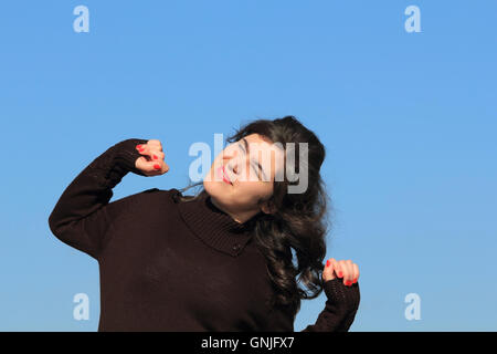 Mujer joven estirando los brazos afuera, en el cielo azul