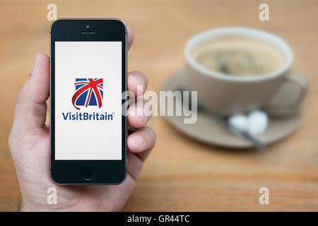 Un hombre mira el iPhone que muestra el logotipo de Visit Britain (uso Editorial solamente). Foto de stock